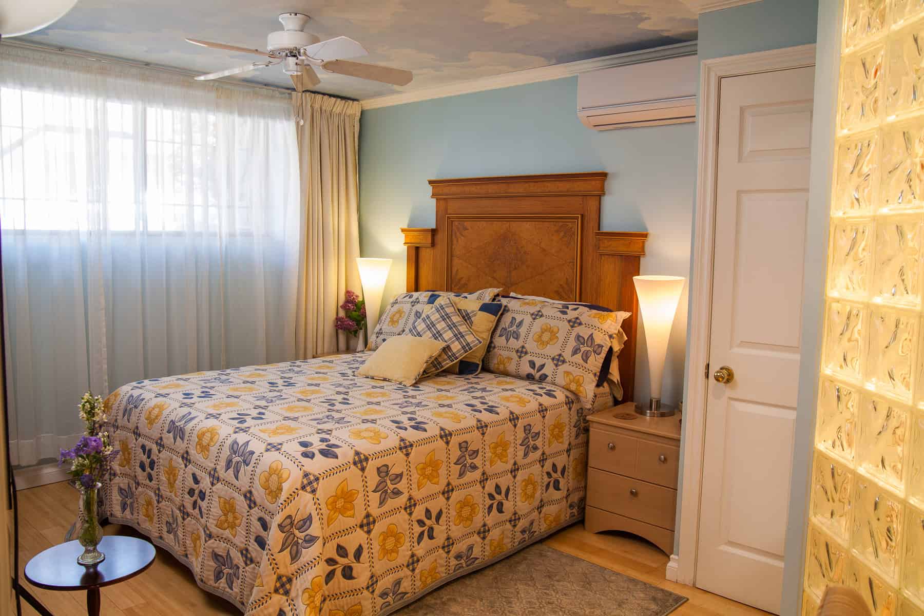 Comfortable bedroom with wooden furniture and floral bedding, bright natural light, and cozy decor.